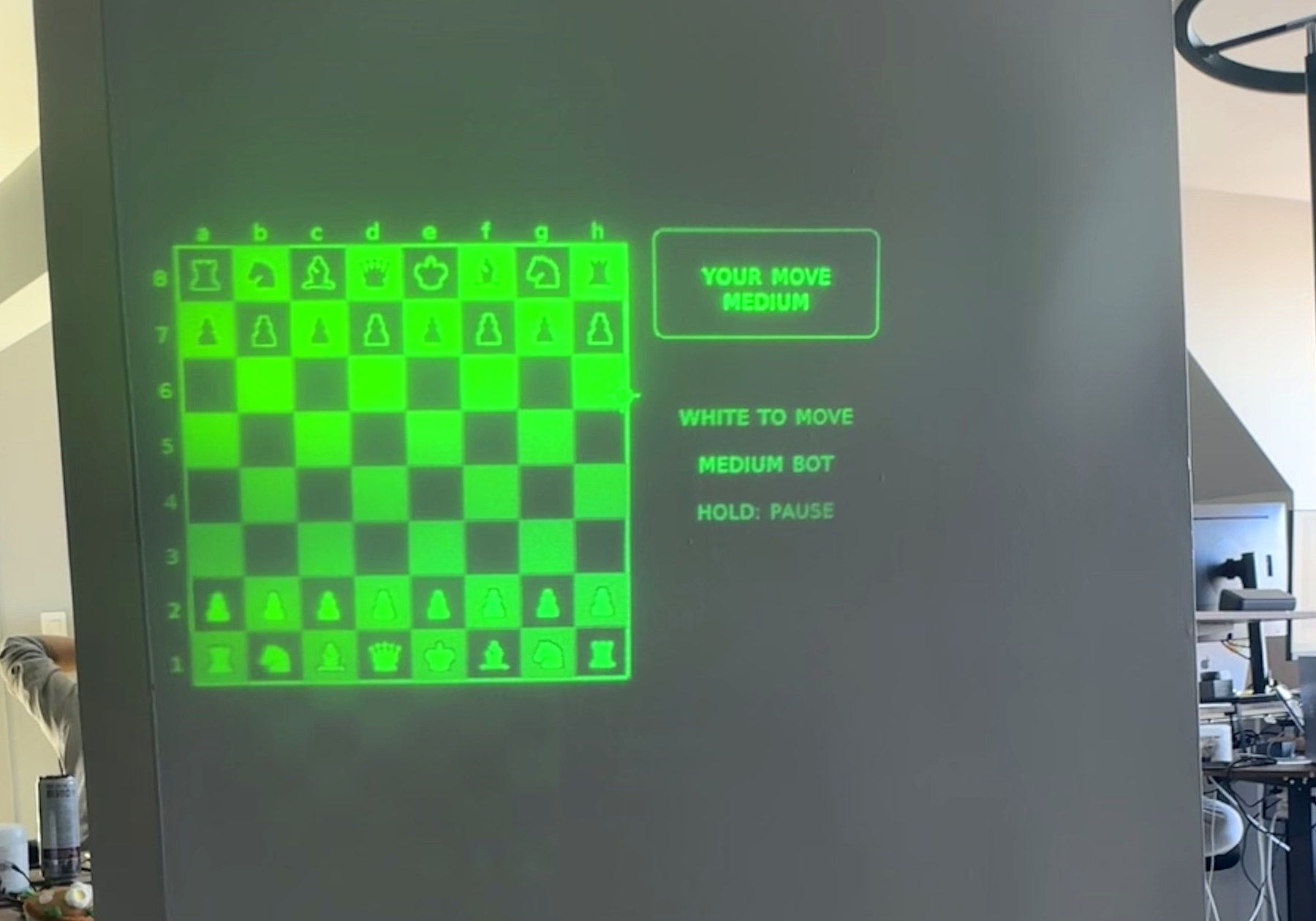 A green chess board and controls from a MIRA app displayed against an office wall